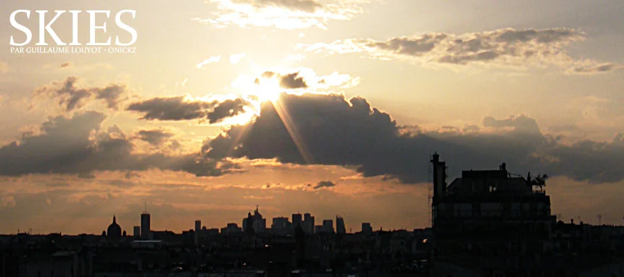 Panorama urbain sous un ciel traversé de rayons de soleil.