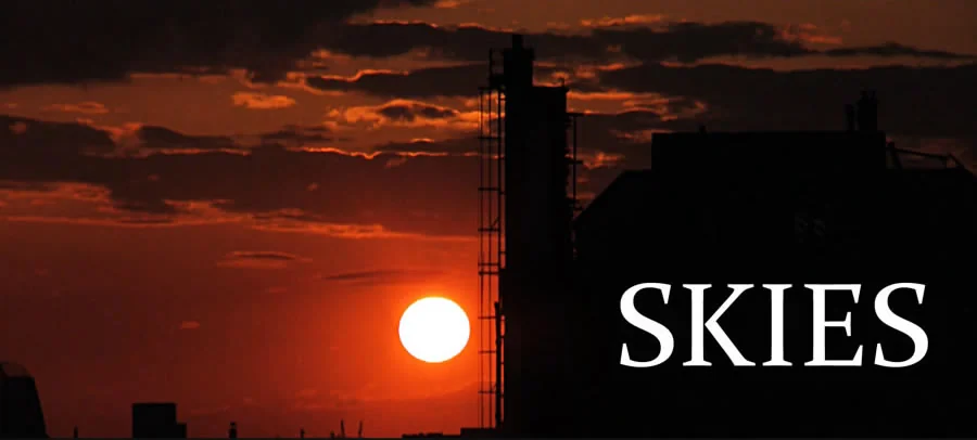 Skies : titre du film sur un coucher de soleil derrière les toits.